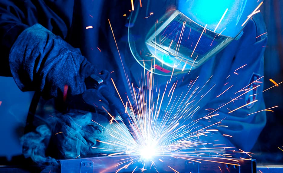 Welder fabricating metal with tools in shop